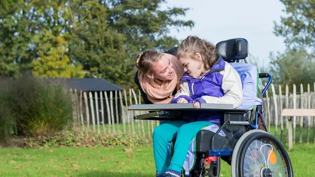 Young girl in wheelchair with carer. Spinal injury care